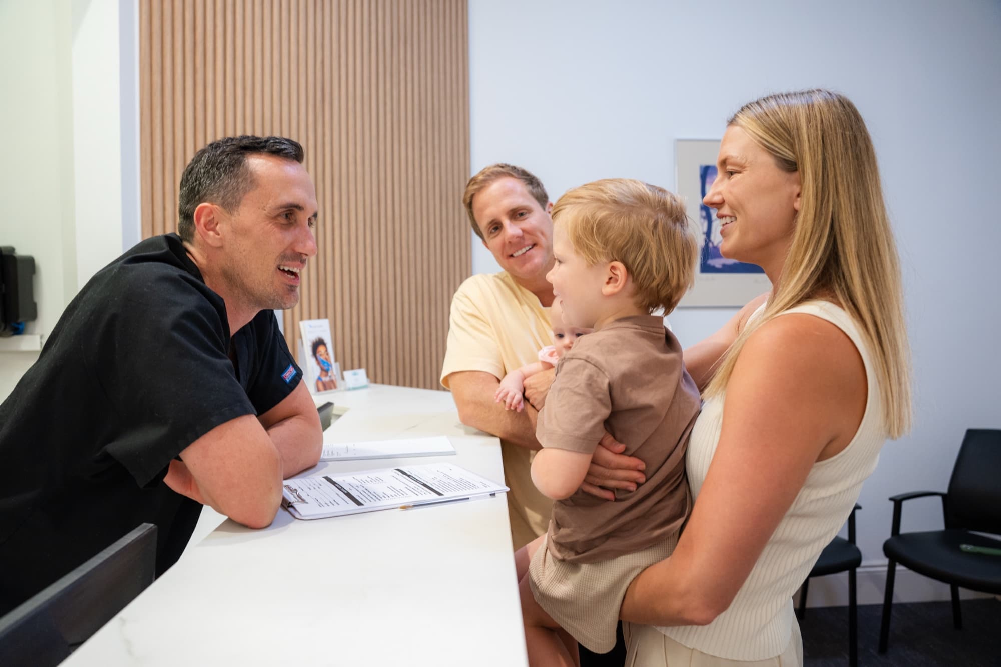 Dr James Bakker greeting a young family with their toddler at the reception desk